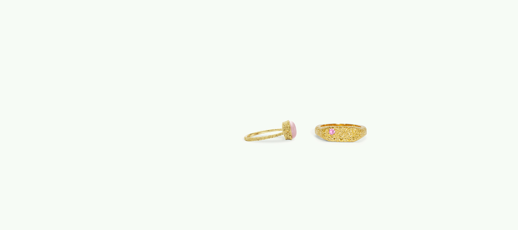 Two pink stone gold rings on a slightly green background in a studio.